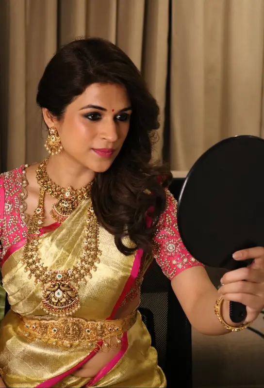 Woman in a gold saree and pink blouse holding a mirror