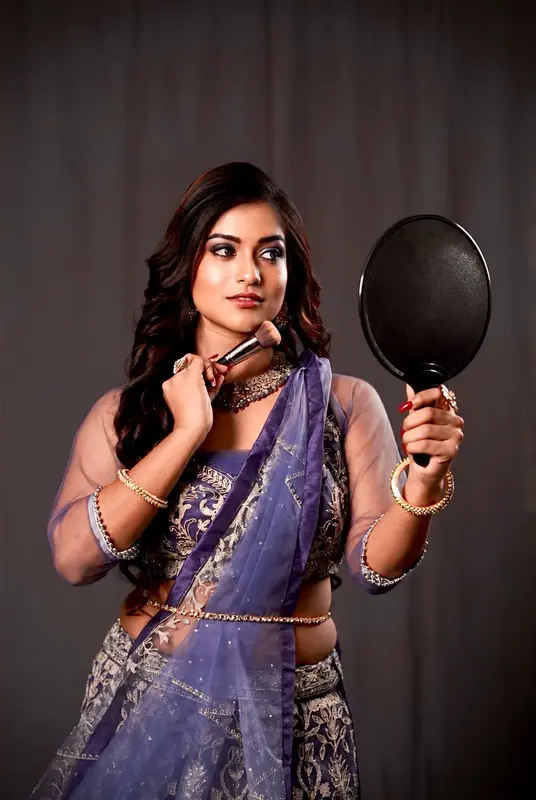 Woman in a blue saree holding a mirror against a dark background