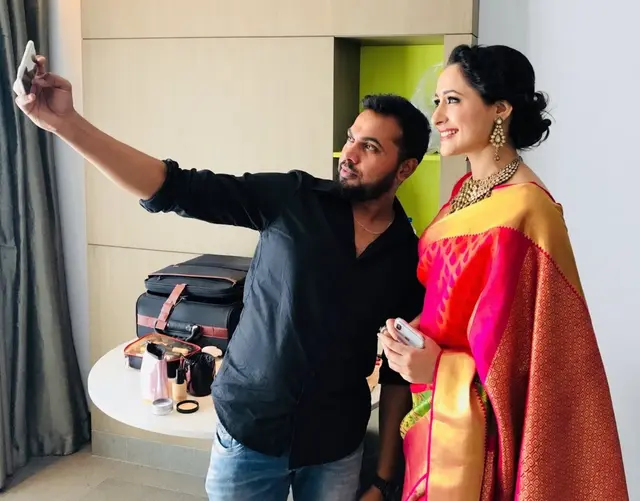 Man and woman in a colourful saree taking a selfie in a makeup room